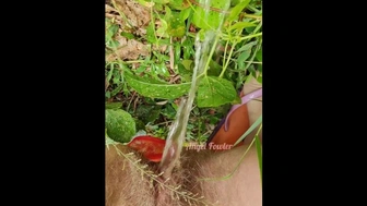 Village woman in a red tunic is pissing in the middle of a green field
